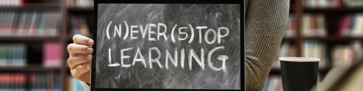 na ekranie komputera czarna tablica z tekstem napisanym białą kredą "(n)ever (s)top learning". Za komputerem siedzi kobieta