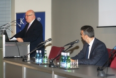Ambasador Pejovic siedzi przy stole prezydialnym. Dyrektor Pastwa stoi przy mównicy.