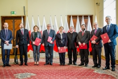 Członkowie Rady Służby Publicznej stoją na tle flag Polski.
