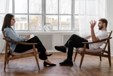 dwie osoby siedzą na fotelach na przeciwko siebie 