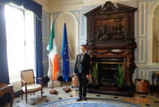 Słuchaczka KSAP stoi w pokoju na tle kominka i flag Irlandii i UE