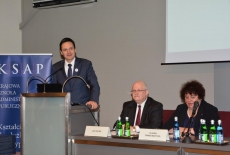 Minister Jacek Cichocki przemawia na mównicy, a przy stole prezydialnym siedzą od lewej: Dyrektor Jan Pastwa, Szef Służby Cywilnej Claudia Torres-Bartyzel