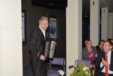Absolwent Wacław Turek stoi z akordeonem w rękach po lewej stronie i kłania się widowni siedzącej na krzesłach w sali po koncercie