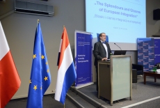 Dyrektor KSAP Wojciech Federczyk stoi przy mównicy i przemawia. Obok stoją flagi Polski, UE, i Holandii