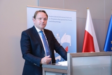 komisarz przy mównicy, w tle flagi polska i unijna