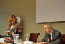  Ewa Junczyk-Ziomecka stoi z otwartą książką w ręku, a obok siedzi Eugeniusz Smolar