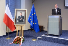 Dyrektor KSAP przemawia przy mównicy, obok stoi portret Władysława Stasiaka