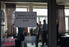 Biała kartka z napisem "Konsultacje ze słuchaczami KSAP" przyklejona do drzwi wejściowych do sali. W tle niewyraźne postaci.
