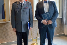 Dyrektor KSAP i Rektor Wyższej Szkoły Policji w Szczytnie po podpisaniu porozumienia stoją na tle flag i sztandaru KSAP