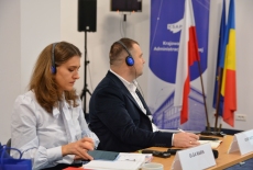 dwoje uczestników siedzą przy stole, pani i pan mają założone słuchawki na uszy