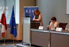 Ewa Junczyk-Ziomecka przemawia przy mównicy a Janina Ochojska siedzi przy stole prezydialnym.