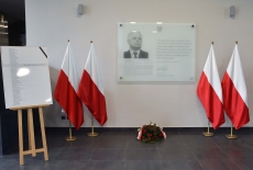 tablica upamiętniająca Patrona Szkoły, obok polskie flagi oraz tablica z listą ofiar katastrofy smoleńskiej