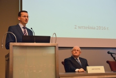 Wiceprezes Rady Ministrów, Minister Rozwoju Mateusz Morawiecki stoi przy mównicy podczas wystąpienia, z lewej stony siedzi Dyrektor KSAP Jan Pastwa.