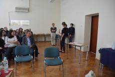 Uczestnicy spotkania siedzą w sali podczas warsztatów. Jedna uczestniczka chodzi po sali z laską dla niewidomych.