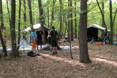 Grupa słuchaczy KSAP stoi i rozmawia na tle namiotów w lesie