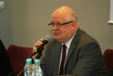 Dyrektor Krajowej Szkoły Administracji Publiczej Jan Pastwa siedząc w czerwonym fotelu mówi do mikrofonu.