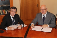 Dyrektor Jan Pastwa i Dobromir Dowiat-Urbański podpisują porozumienie przy stole.