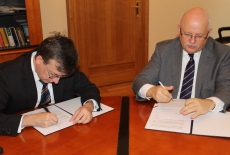Dyrektor Jan Pastwa i Dobromir Dowiat-Urbański podpisują porozumienie przy stole.