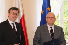 Dyrektor Jan Pastwa i Dobromir Dowiat-Urbański po podpisaniu porozumienie stoją na tle flag Polski i UE.