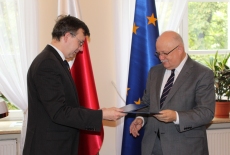 Dyrektor Jan Pastwa i Dobromir Dowiat-Urbański po podpisaniu porozumienie stoją na tle flag Polski i UE i podają sobie ręce.