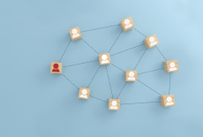 Drewniane kostki z białymi ikonami profili połączone przerywanymi liniami tworzą sieć relacji; jedna kostka z czerwoną ikoną wyróżnia się na tle pozostałych.