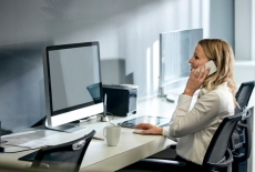 kobieta siedzi przy biurku z komputerem i rozmawia przez telefon