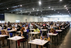 Kandydaci pochyleni nad biurkami piszą egzamin, widok na całą salę egzaminacyjną. 