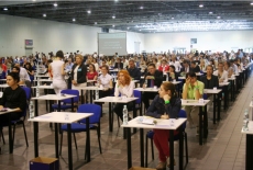 Sala egzaminacyjna, kandydaci siedzą przy stolikach i czekają na rozpoczęcie egzaminu.