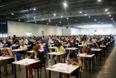 uczestnicy egzaminu siedzą przy pojedynczych stolikach w dużej hali 