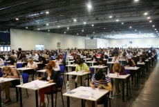 Uczestnicy egzaminu do postępowania kwalifikacyjnego w służbie cywilnej siedzią przy pojedynczych stolikach na hali egzaminacyjnej.
