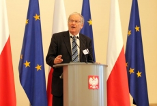 Pan przemawia na mównicy na tle flag Polski i UE