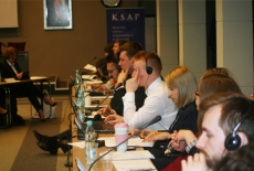 Uczestnicy siedzą przy stole zasłuchani, korzystają ze słuchawek.