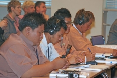 Uczestnicy szkolenia siedzą w ławkach ze słuchawkami na głowie