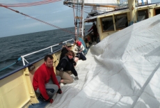 Pięcioro uczestników rejsu zwija żagiel na pokładzie żaglowca.