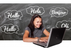 dziewczyna siedzi przed otwartym laptopem, w tle na czarnej tablicy napisy w różnych językach