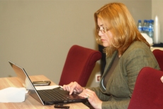 Uczestniczka programu siedząc przy stole pisze przy komputerze.