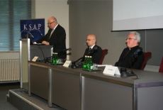Dwie osoby siedzące za stołem na podium. Z lewej Arcybiskup Migliore. Dyrektor Jan Pastwa przemawia stojąc z prawej strony podium.