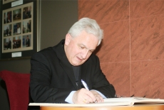 Jego Ekscelencja abp Celestino Migliore siedząc przy stole wpisuje się do księgi pamiątkowej.