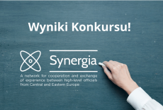 dłoń pisząca kredą na tablicy, napis - Wyniki konkursu, Synergia A network for cooperation and exchange of experience between high-level officials from Central and Eastern Europe