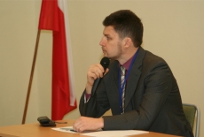 Uczestnik seminarium przemawia do mikrofonu. Za nim flaga Polski.
