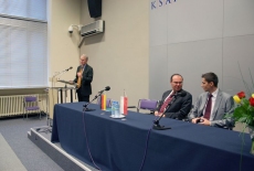 Pan Ambasador stoi przy mównicy i mówi do mikrofonu obok przy stole prezydialnym siedza przedstawiciele KSAP