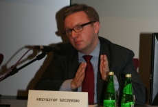 Pan Krzysztof Szczerski siedzi przy stole i mówi do mikrofonu