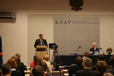 Bronisław Komorowski stoi na mównicy i przemawia obok siedzi przy stole Jacek Czaputowicz Dyrektor KSAP