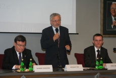 Mirosław Stec stoi i mówi do mikrofonu, obok siedzą Paweł Banaś oraz Sławomir Brodziński