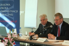 Bogusław Wind mówi do mikrofonu obok niego siedzi Jacek Czaputowicz