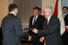 Sławomir Brodziński oraz Dyrektor KSAP wręczają absolwentowi dyplom, za nimi stoi poczet sztandarowy