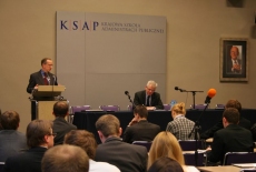 Pan Jan Tombiński stoi przy mównicy i przemawia obok przy stole siedzi Dyrektor KSAP