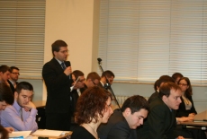 Uczestnik spotkania stoi i mówi do mikrofonu, obok siedzą inni uczestnicy