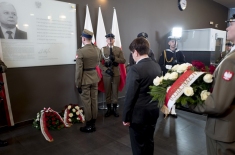 Premier Beata Szydło, w asyście wojskowej, składa kwiaty pod tablicą pamiątkową. 