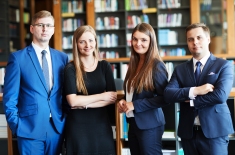 Czterech słuchaczy (dwie panie w środku i dwóch panów) stoją w bibliotece na tle regałów z książkami